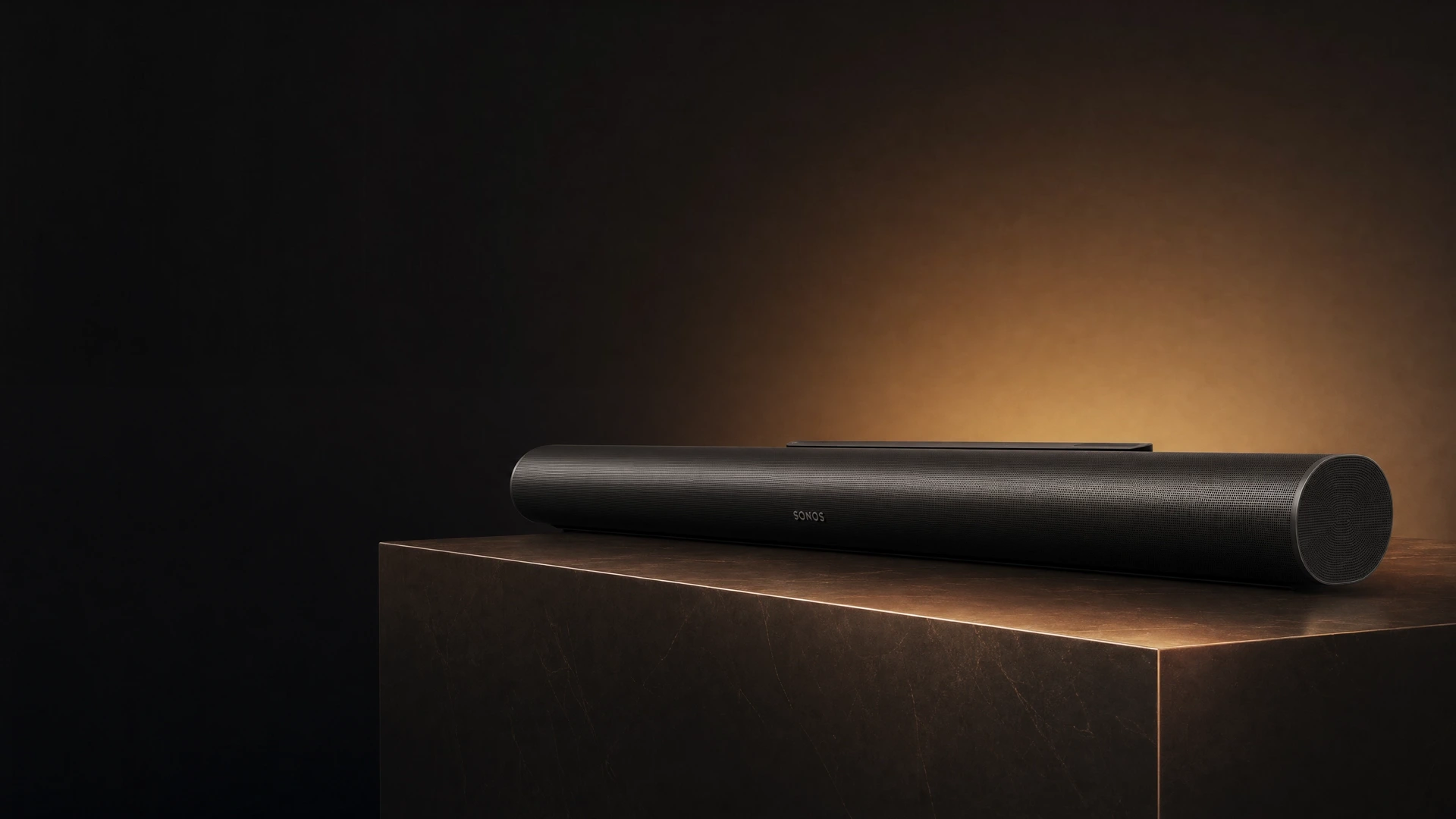 Black Sonos Arc Ultra on a bronze stone plinth against a warmly lit studio backdrop